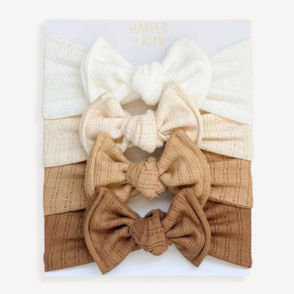 Set of white and brown top knot fabric baby bows on a branded card held by a hand.