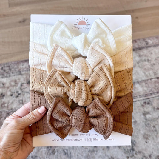 Set of white and brown top knot fabric baby bows on a branded card held by a hand.