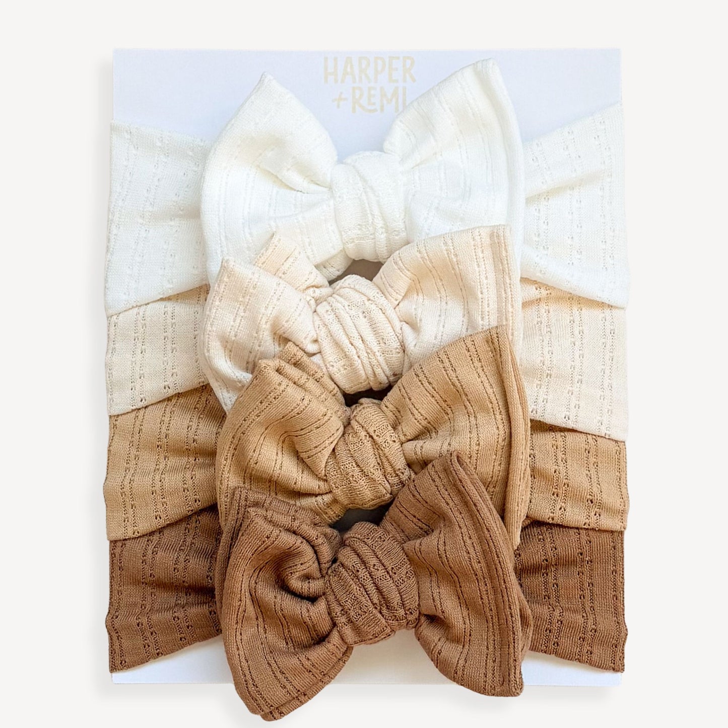 Set of pointelle knit textured baby bows in various neutral colors on a card held by a hand.