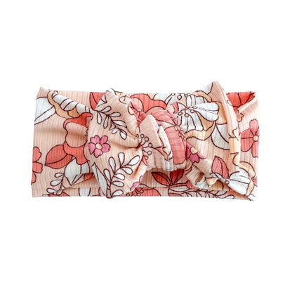 Oversized bow baby headband in coral large floral print, crafted from ribbed knit fabric, displayed on a white background