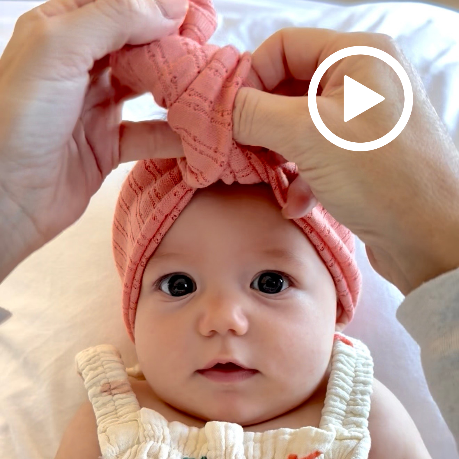 Baby wearing a coral pink headband with hands adjusting it, on a white background
