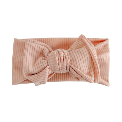 Oversized bow baby headband in dusty pink, crafted from ribbed cotton jersey knit fabric, displayed on a white background