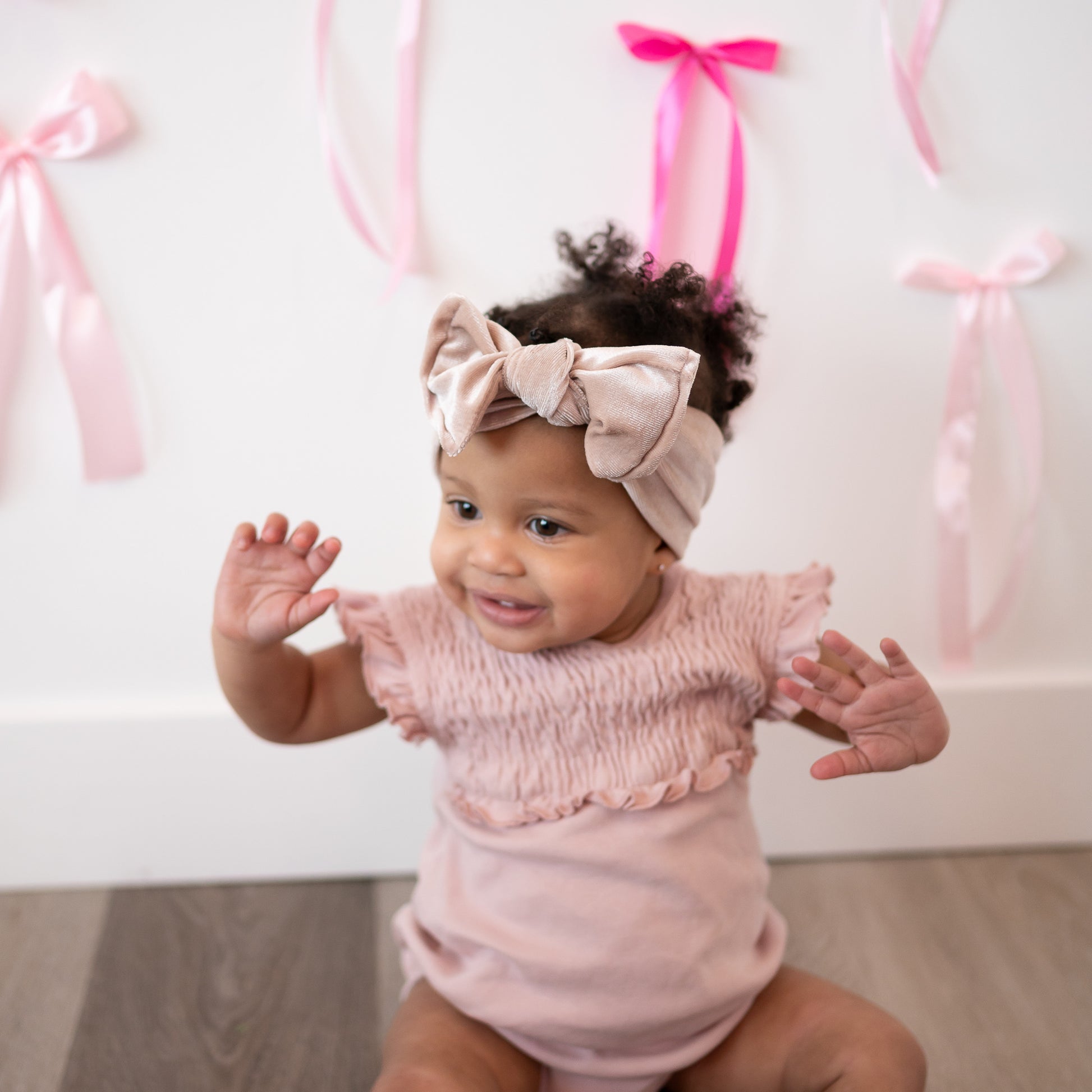 Baby wearing a pink outfit and headband with pink ribbons in the background