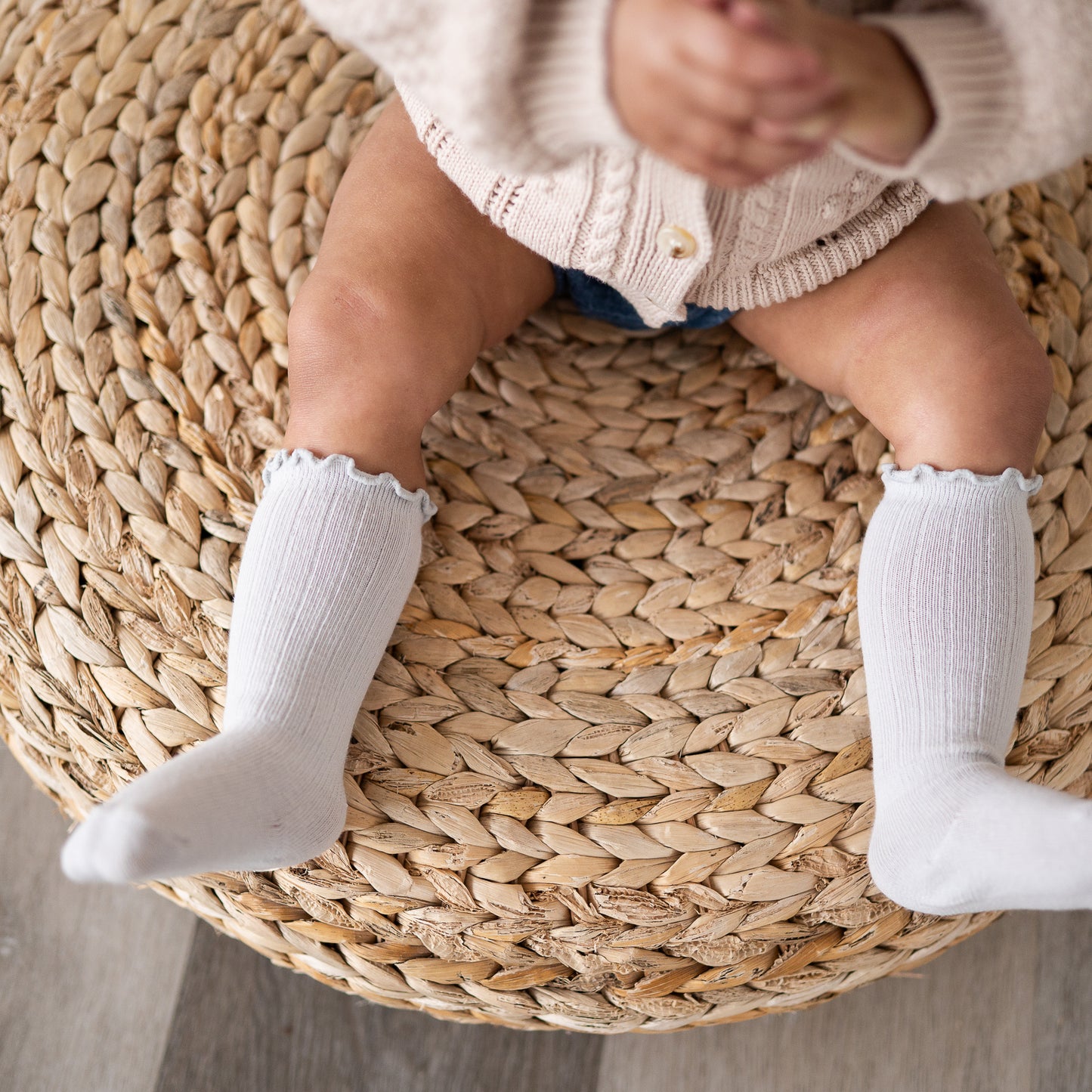 Baby's legs wearing light gray knee socks on a woven stool