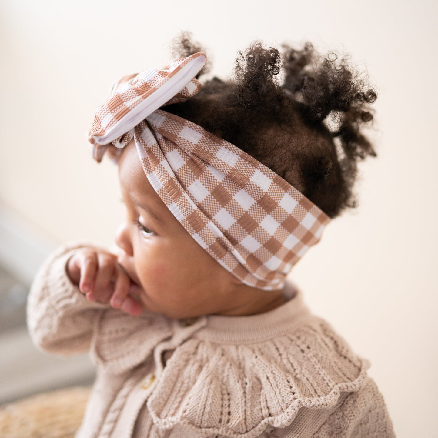 Baby wearing a checkered headband and beige outfit