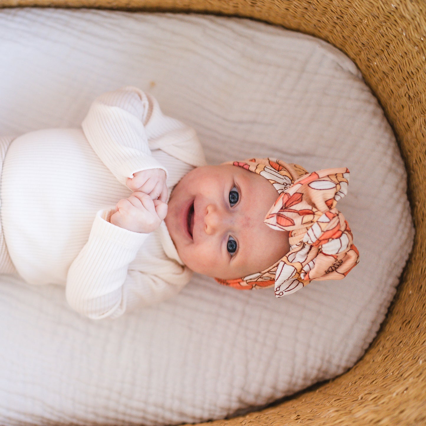 Baby lying in a basket wearing a white outfit and a colorful headband.