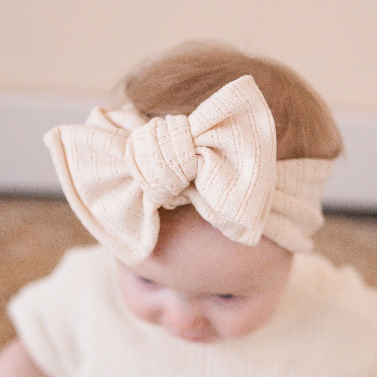 Close up view of a baby girl wearing a beige bow headband with a blurred background.