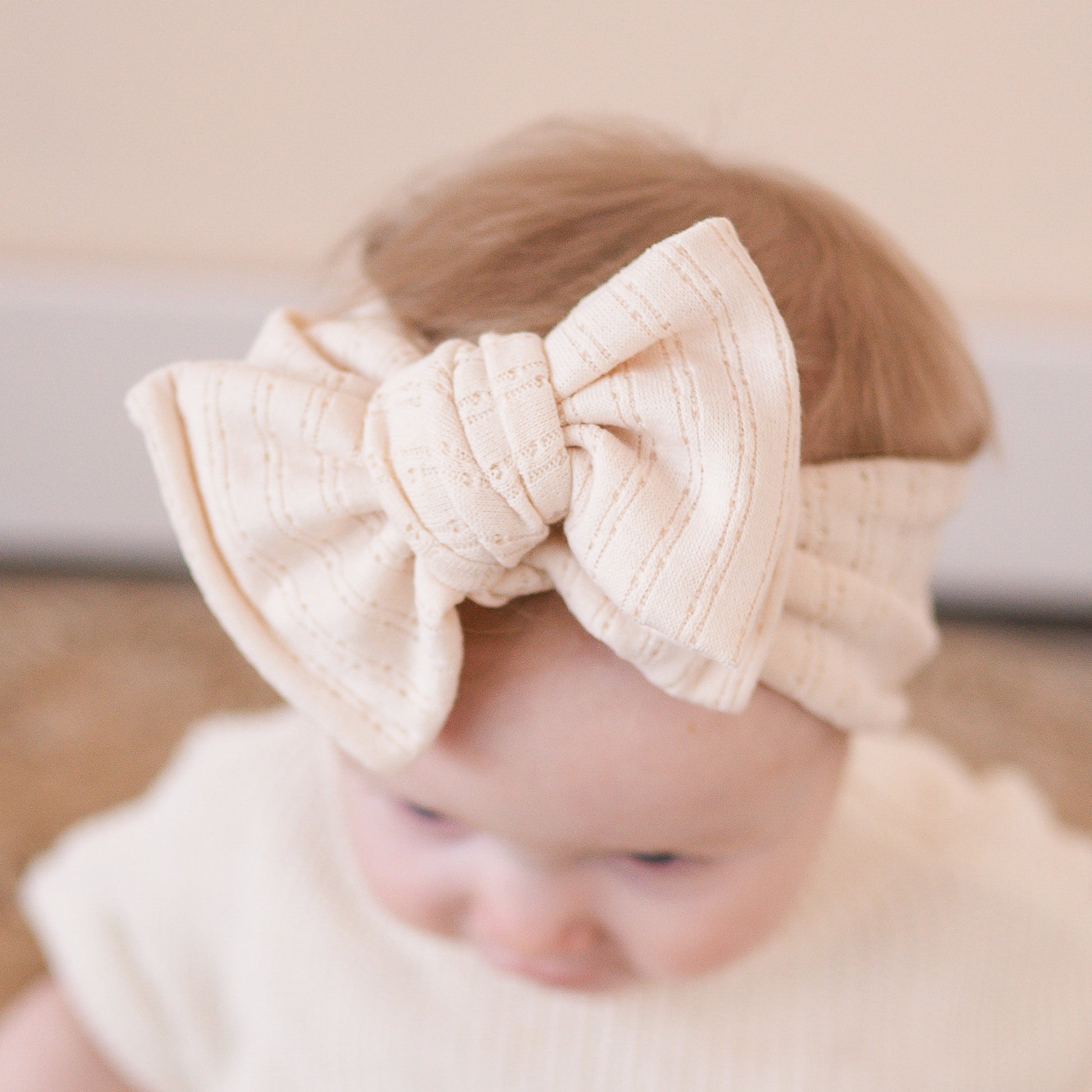 Close up view of a baby girl wearing a beige bow headband with a blurred background.