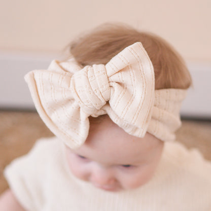 Close up view of a baby girl wearing a beige bow headband with a blurred background.