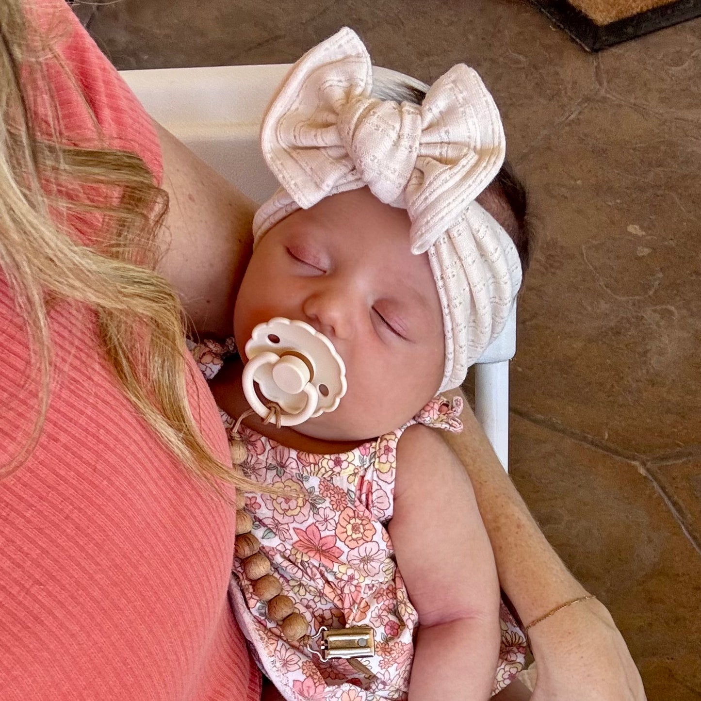Baby wearing a floral outfit and cream pointelle top knot bow headband, held by a person.