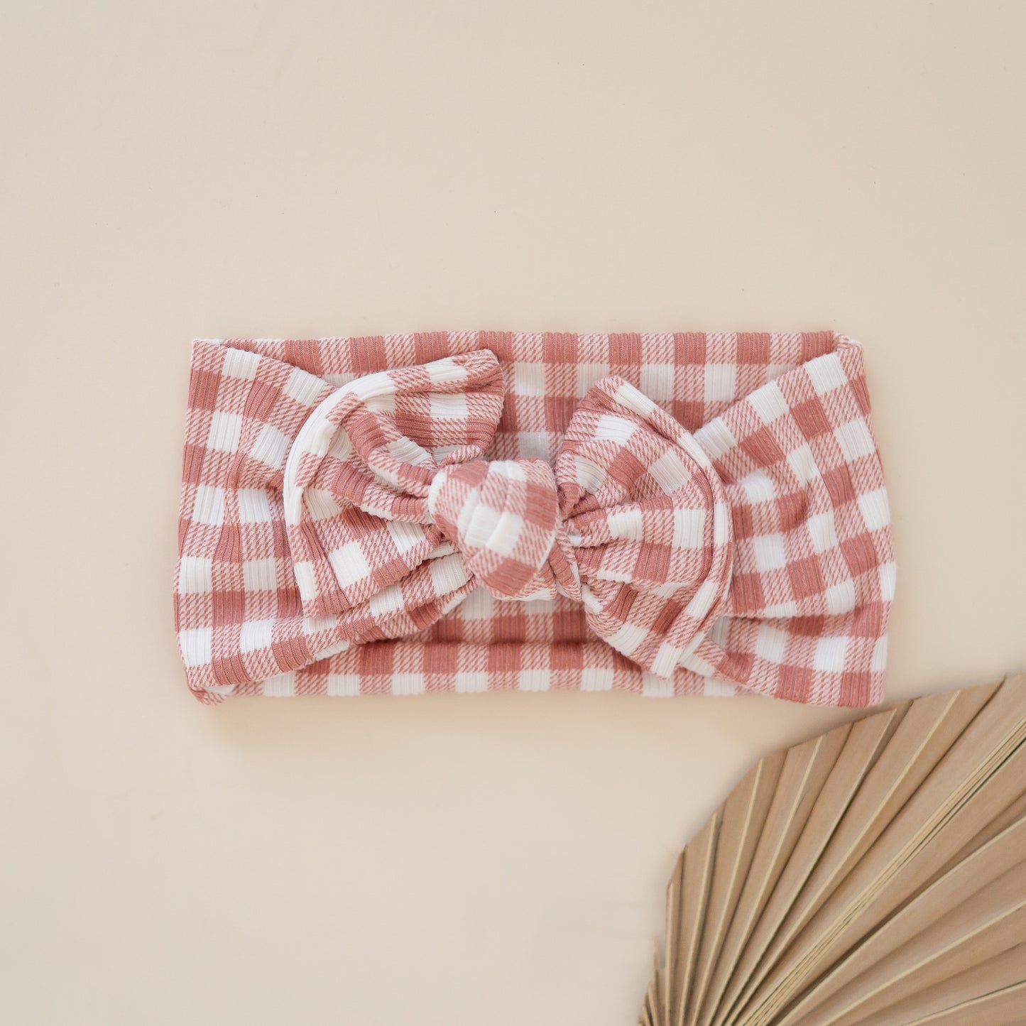 Dusty pink and white gingham checkered headband with a bow on a beige background