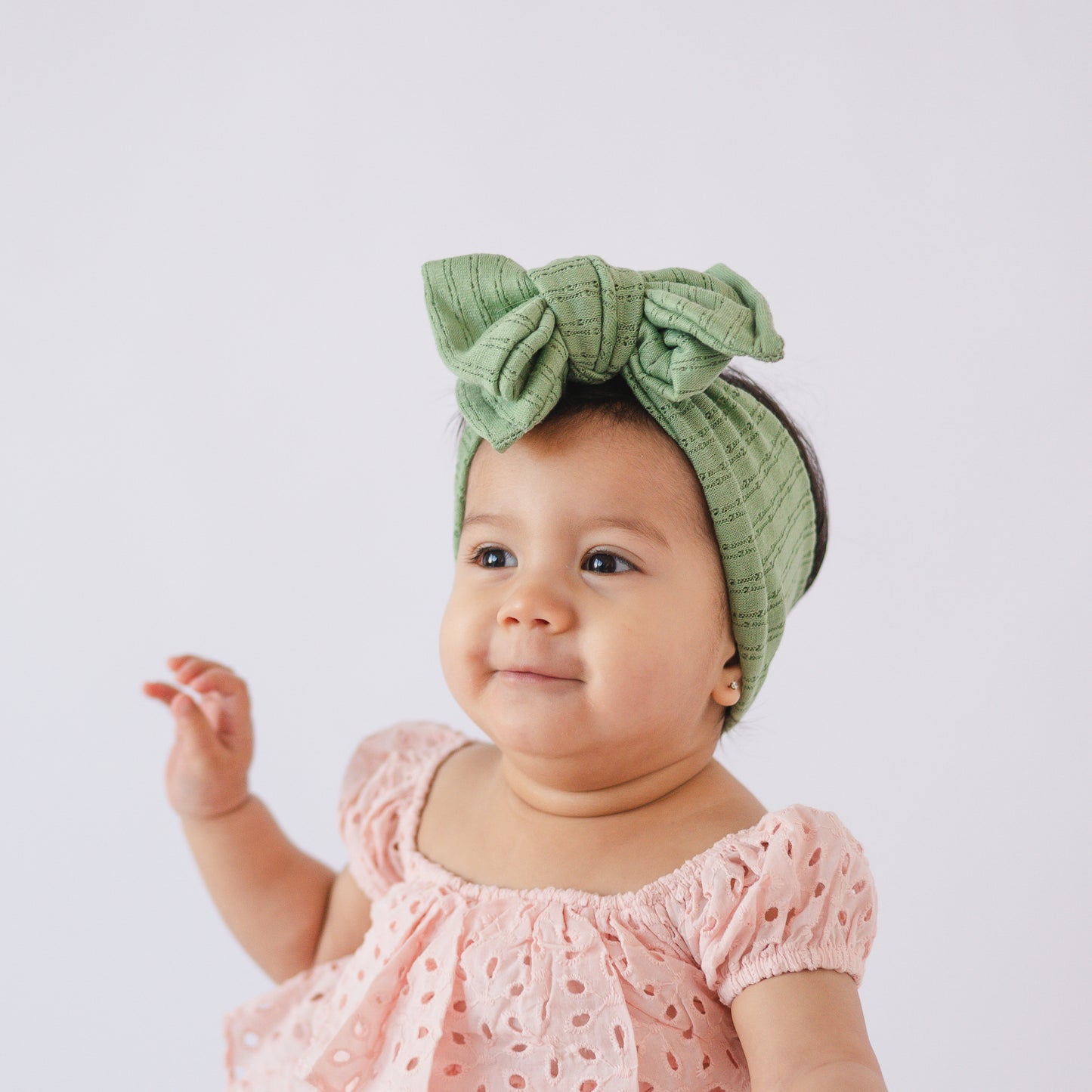 Baby wearing a green oversized bow headband and pink dress on a white background