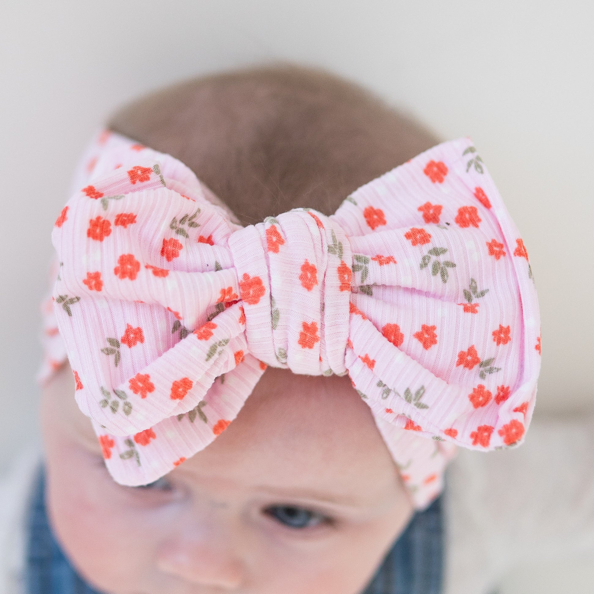 Top detailed view of a baby wearing a pink floral oversized bow headband with a blurred background