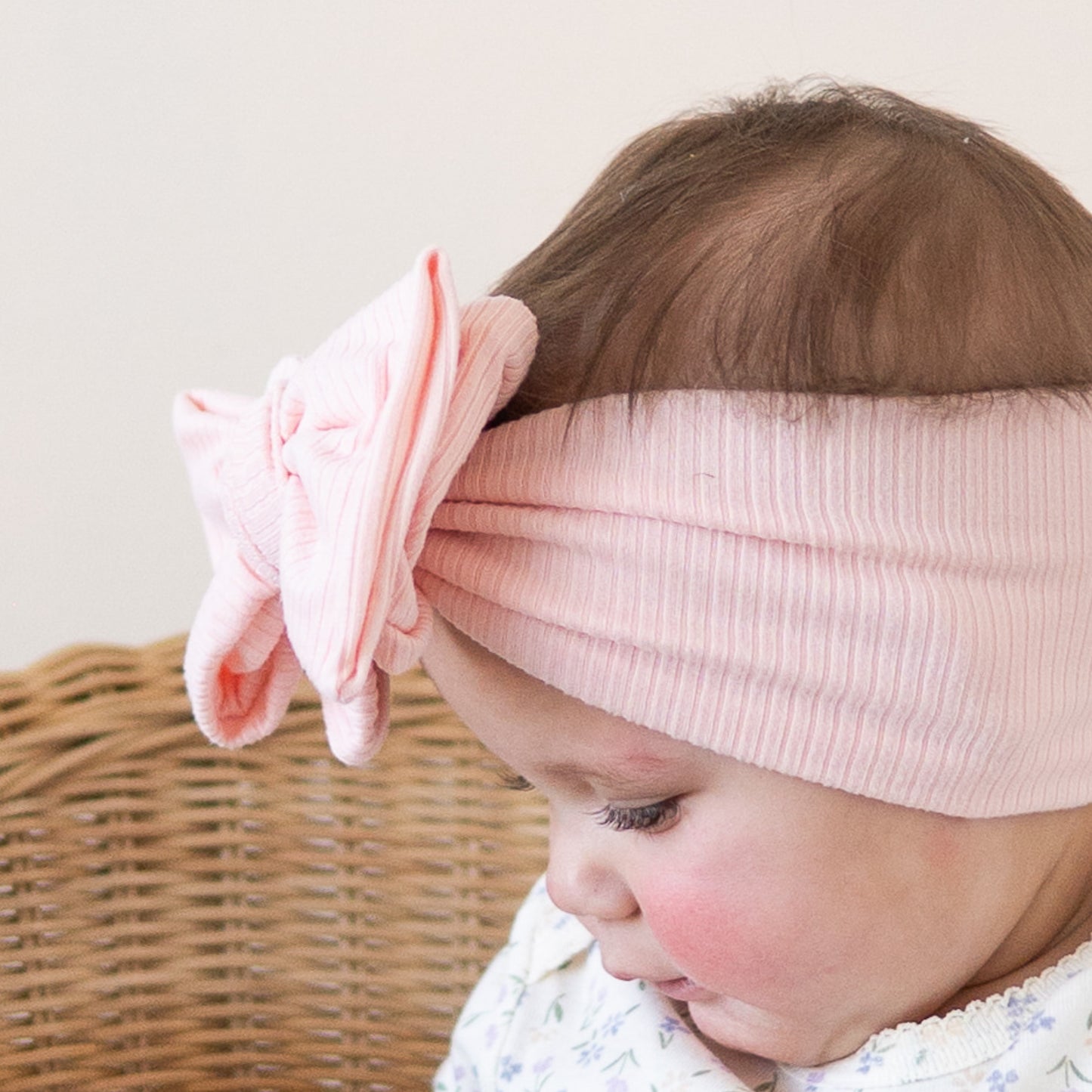 Detail view of baby wearing a pink ribbed oversized bow, looking down.