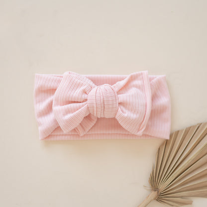 Flat lay of ribbed pink headband with a bow on a beige background