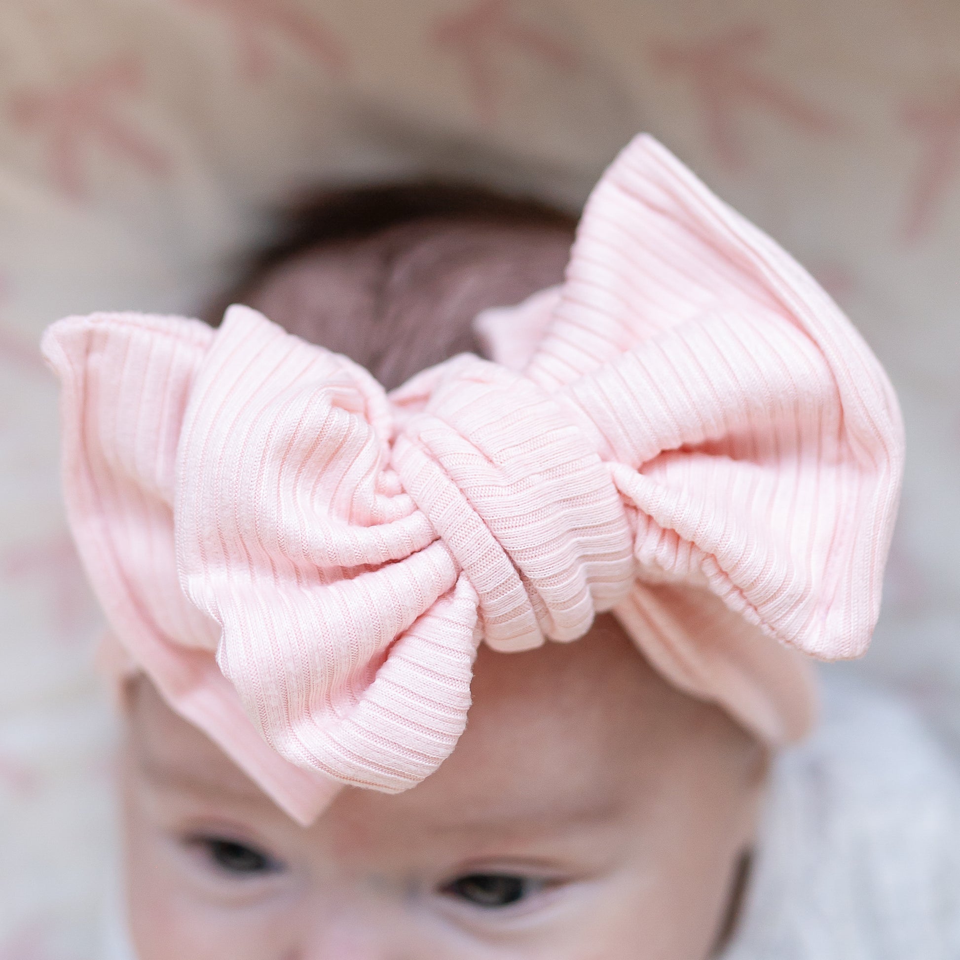 Close-up of a baby wearing a large pink bow headband with a blurred background.