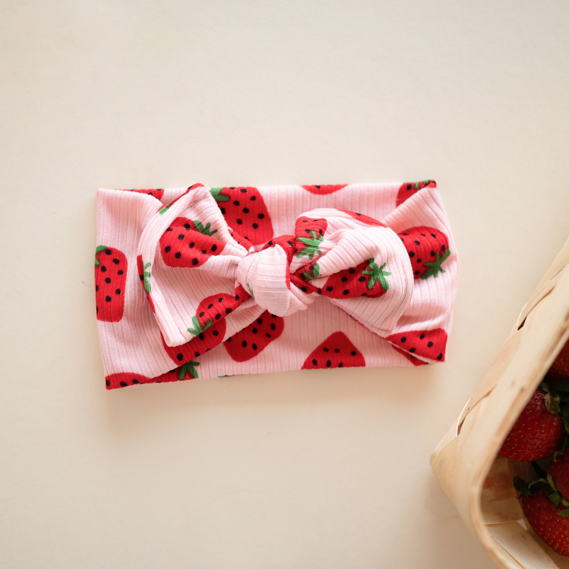 Flat lay of a pink ribbed top knot headband with bright red cherry print.