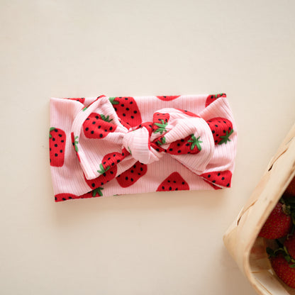 Flat lay of a pink ribbed top knot headband with bright red cherry print.