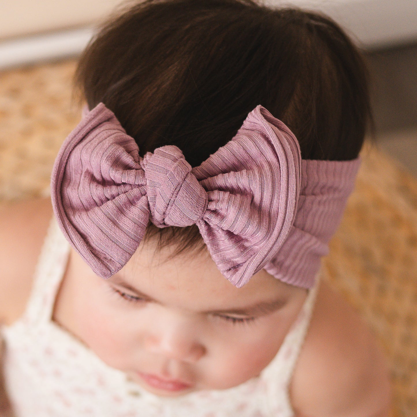 Up close view of a baby wearing a purple top knot bow headband with a blurred background