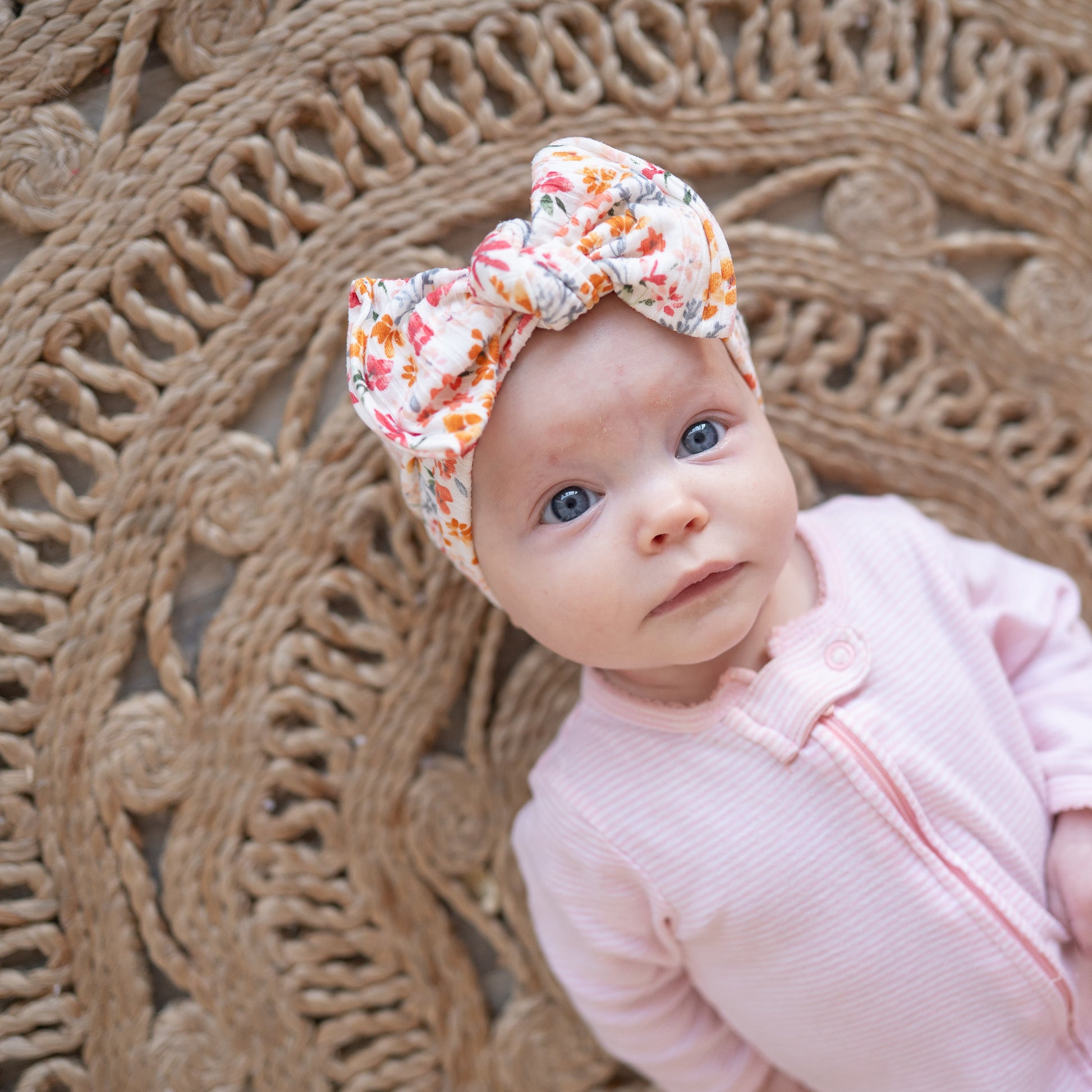 Baby wearing a floral headband and pink outfit against a textured brown background