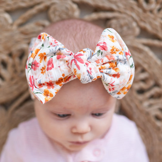 Baby wearing a pink and yellow floral top knot headband with a blurred natural background