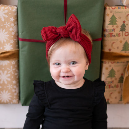 Child wearing a red headband with a bow in front of Christmas presents