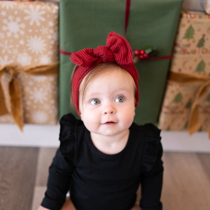 Baby wearing a red headband with a bow in front of Christmas presents