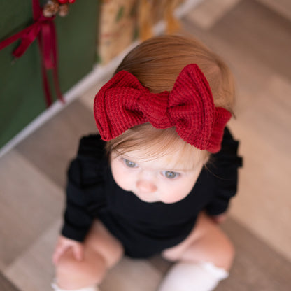 Baby wearing a red bow headband sitting on stairs