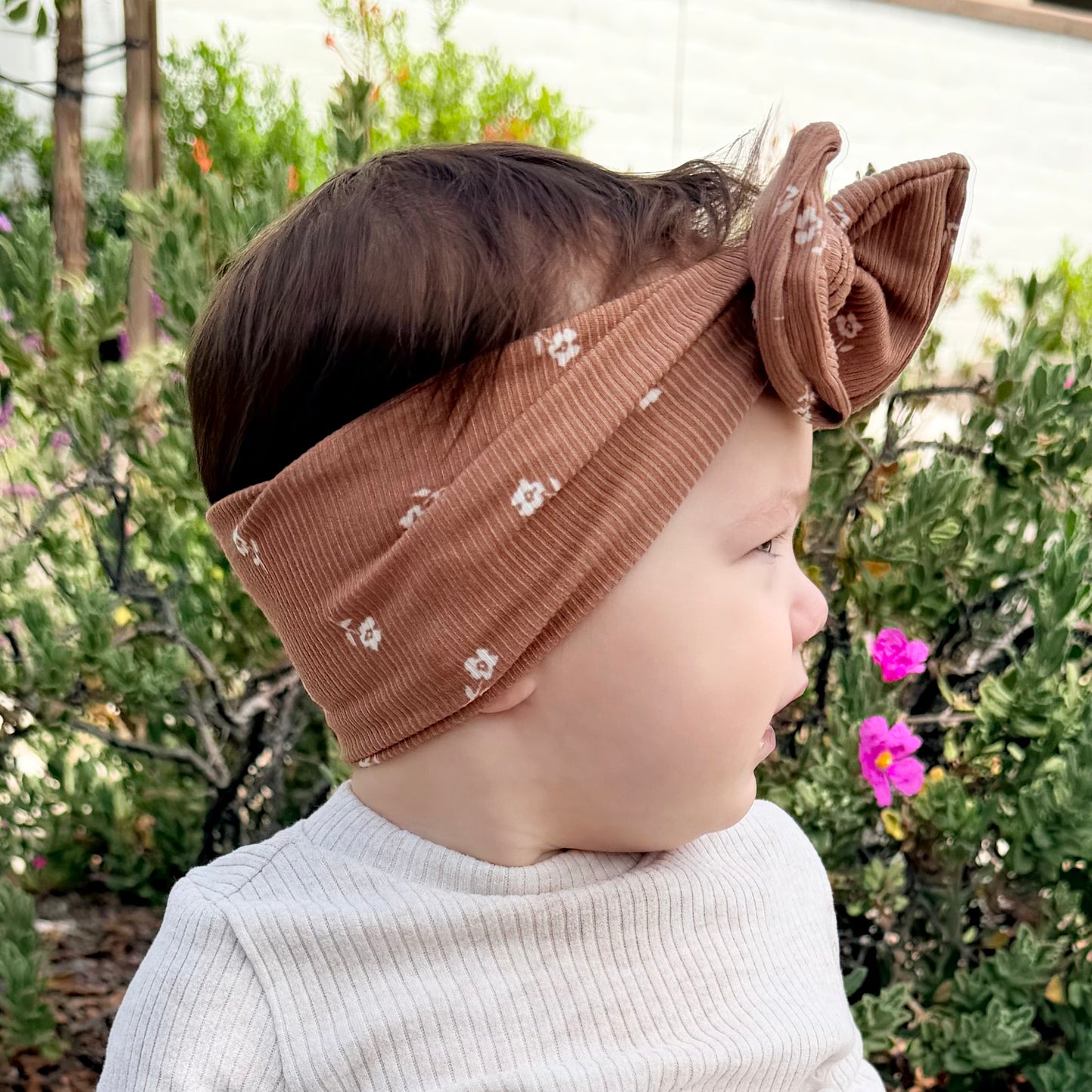 Baby girl wearing a brown top knot headband with floral patterns outdoors