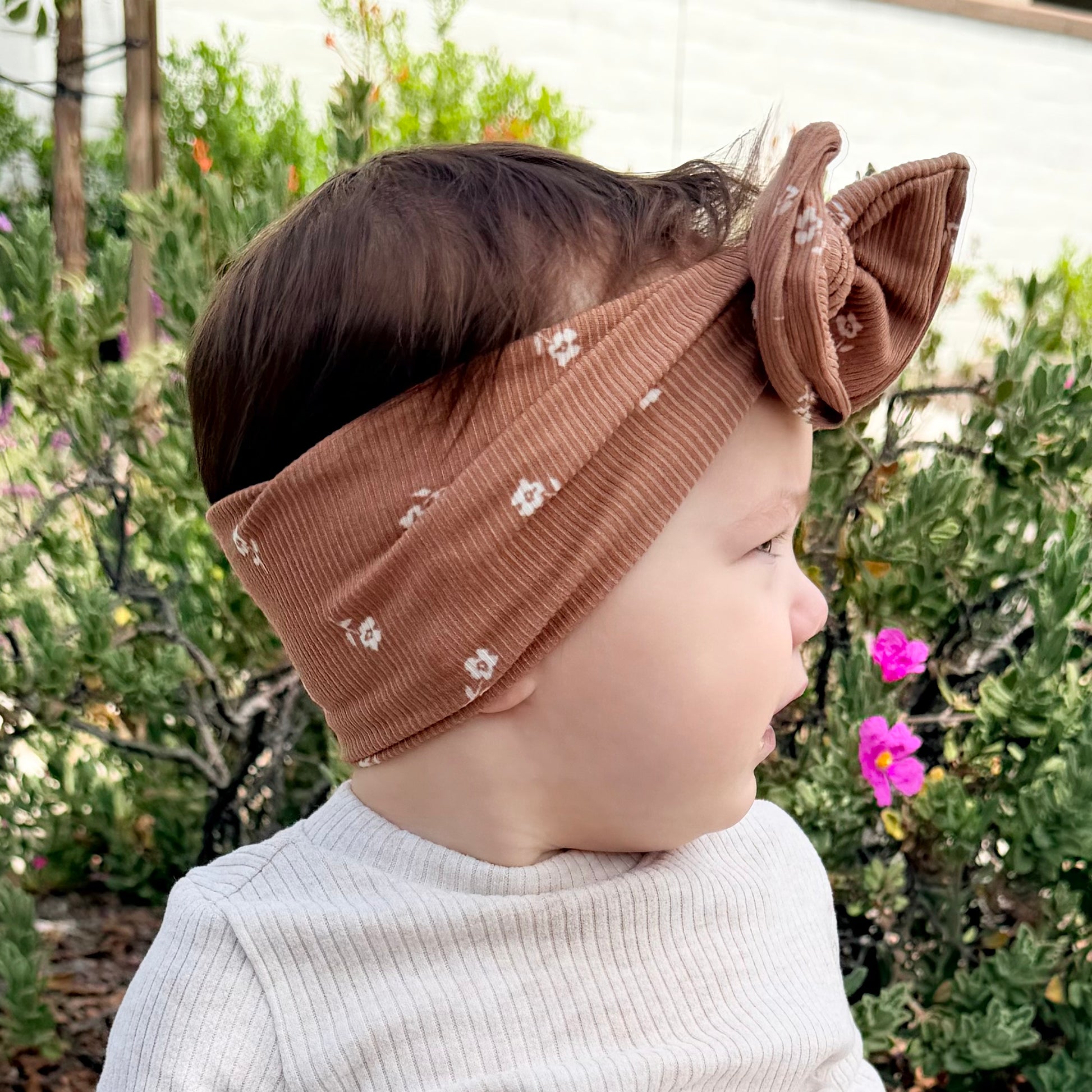Baby girl wearing a brown top knot headband with floral patterns outdoors