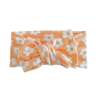 Oversized bow baby headband in orange with white retro daisy print, crafted from cotton jersey knit fabric, displayed on a white background
