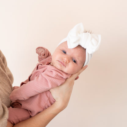 Newborn baby in a pink outfit with a white headband held against a beige background