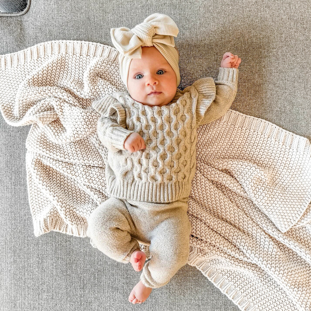 Baby wearing a beige sweater and matching pants, with a beige waffle knit oversized bow.