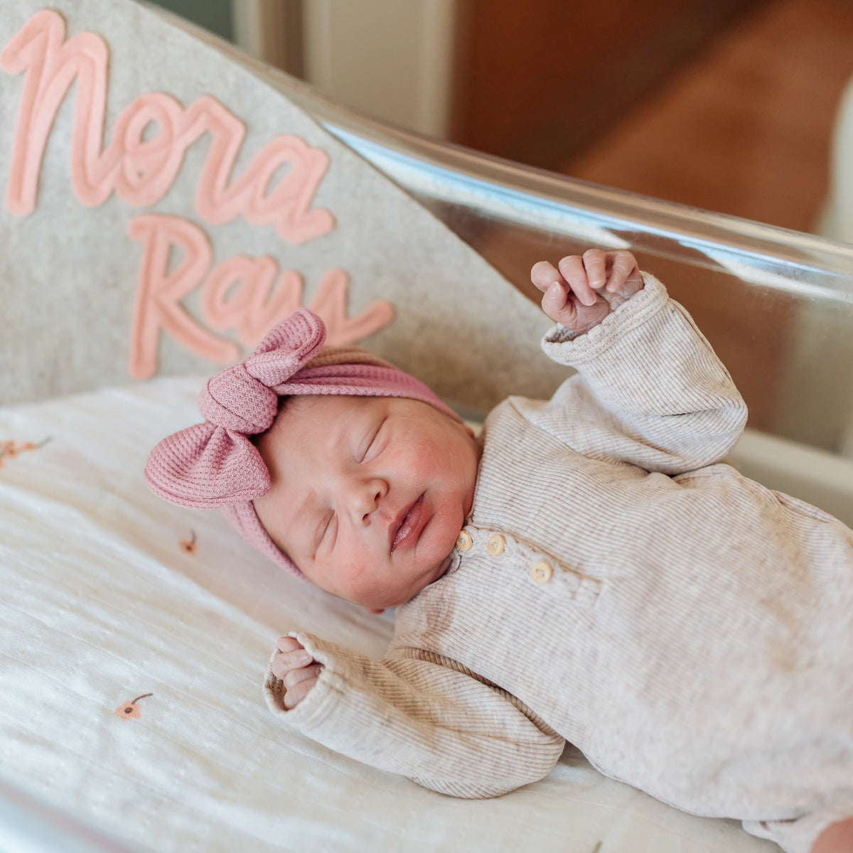 Newborn baby girl sleeping in a hospital cot wearing a pink waffle knit top knot bow.