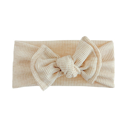 Top knot baby headband in oatmeal (beige) heather, crafted from waffle knit fabric, displayed on a white background