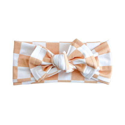 Top knot baby headband in light orange and white checker print, crafted from cotton jersey knit fabric, displayed on a white background