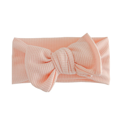Oversized bow baby headband in peachy pink, crafted from waffle knit fabric, displayed on a white background