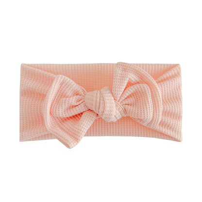 Top knot baby headband in peach toned pink, crafted from waffle knit fabric, displayed on a white background