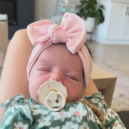 Newborn baby girl sleeping wearing a light pink waffle top knot headband.