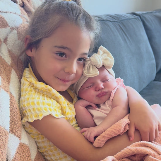Older sister holding newborn baby wearing a oatmeal waffle top knot headband.