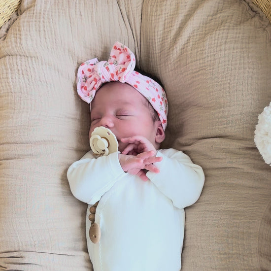 Baby lying on a Snuggle Me, wearing a light pink ribbed top knot bow with floral print.