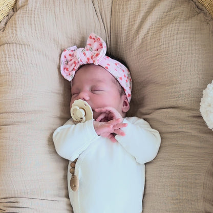 Baby lying on a Snuggle Me, wearing a light pink ribbed top knot bow with floral print.