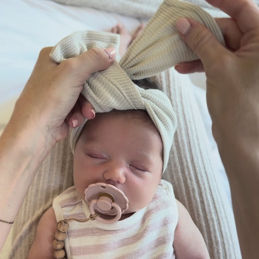 Tutorial showing how to tie a waffle top knot on a newborn's head.