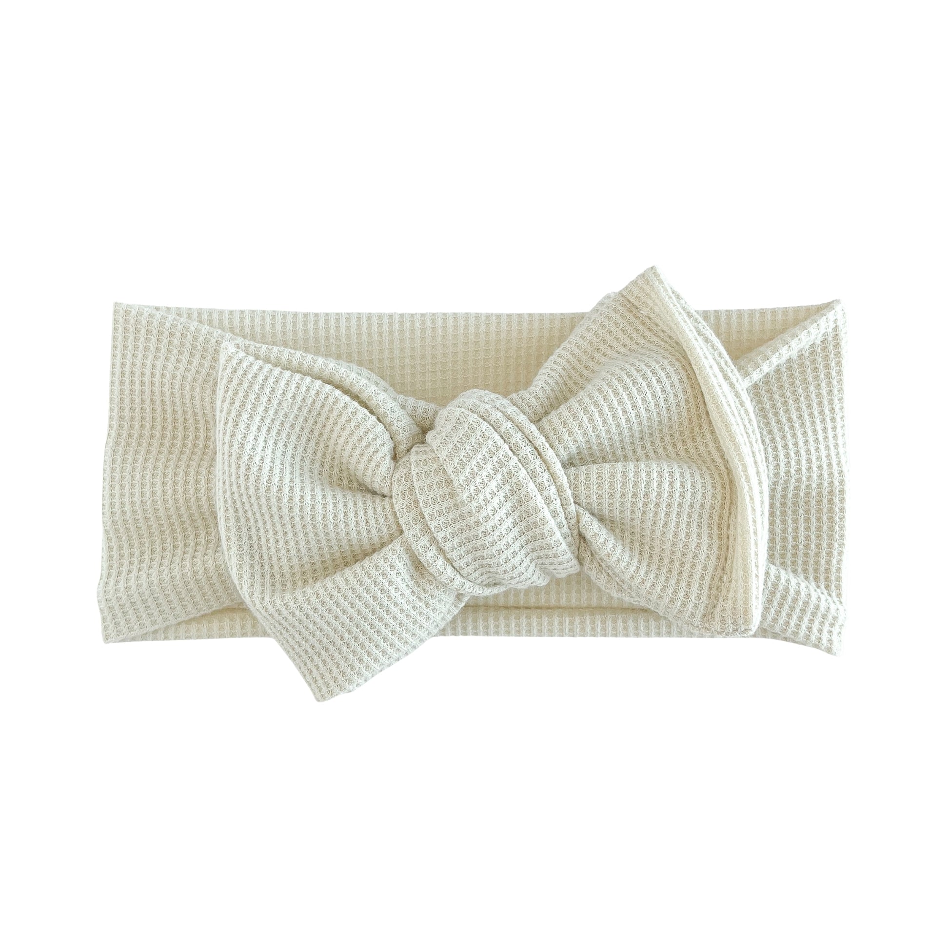 Oversized bow baby headband in sand (beige), crafted from waffle knit fabric, displayed on a white background
