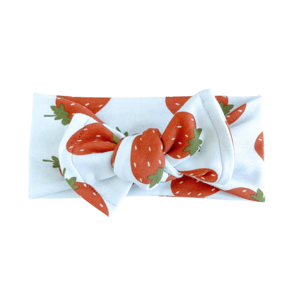 Top knot baby headband in white with red strawberry print, crafted from cotton jersey knit fabric, displayed on a white background