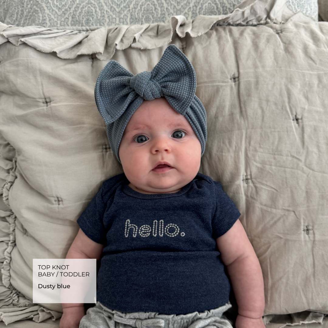 baby wearing a blue waffle top knot bow on a bed.