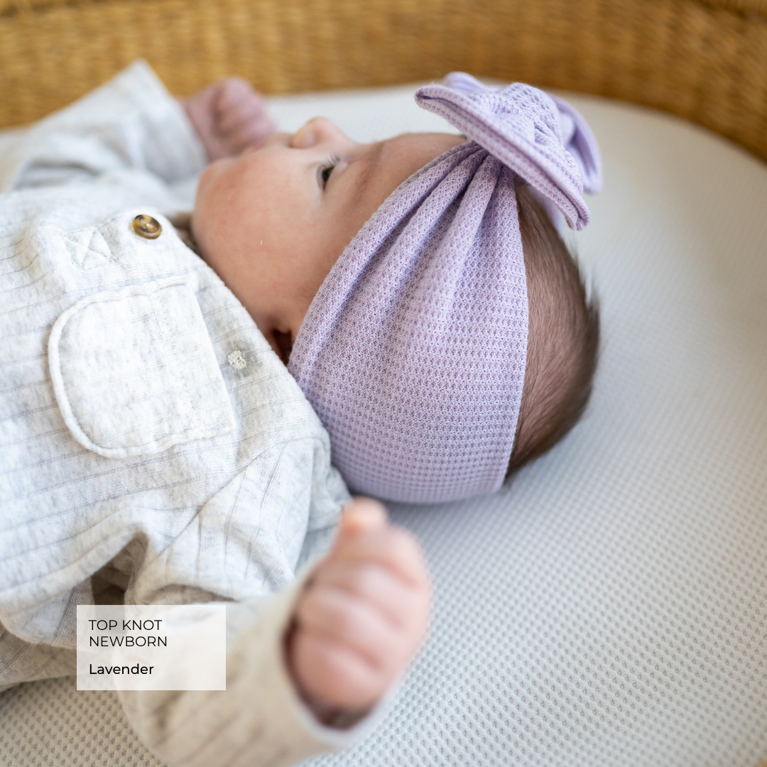 Baby wearing a lavender top knot headband on a neutral background