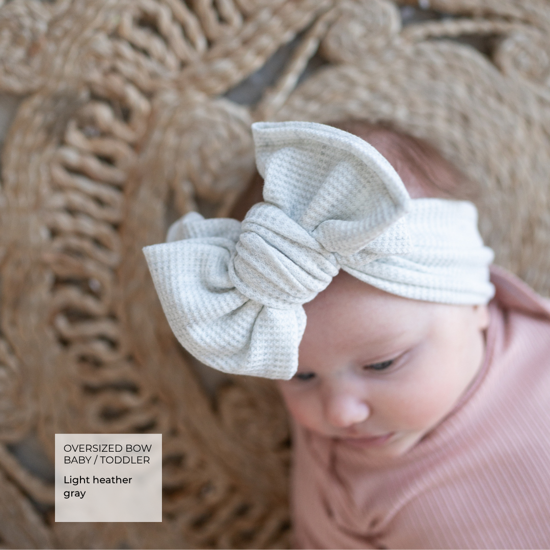 close up of baby laying on rug showing texture of light gray bow.