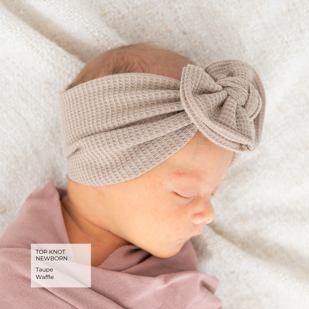 A sleeping newborn baby wearing a taupe waffle-knit top knot headband and a dusty rose blanket, with a text overlay in the bottom left corner.
