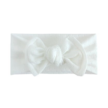 Top knot baby headband in white, crafted from pointelle knit fabric, displayed on a white background